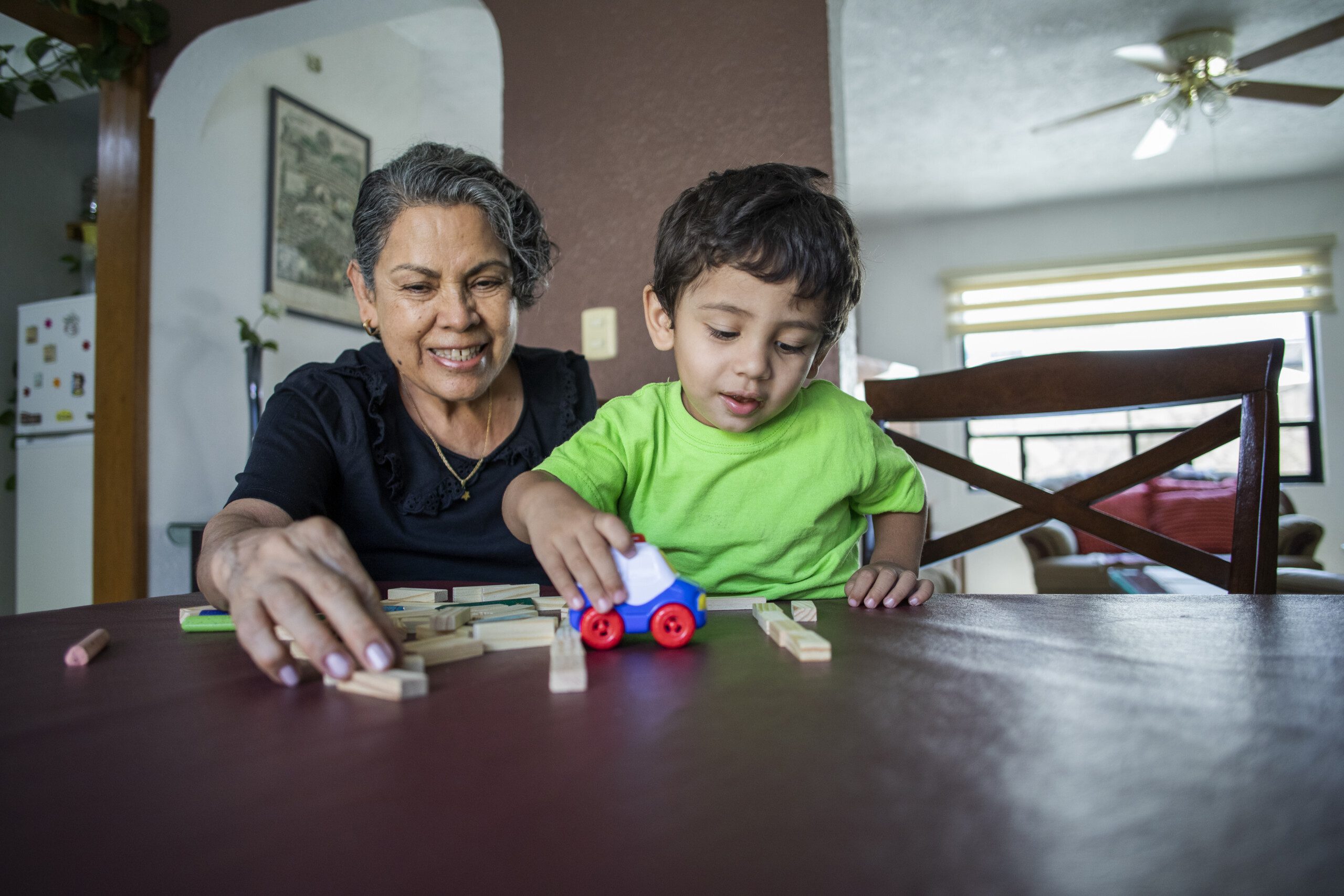 Child playing with a toy car alongside a smiling woman.