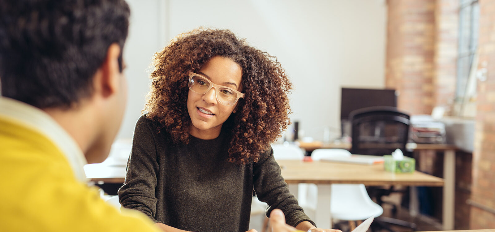 Woman with curly hair speaks to a man in an office.