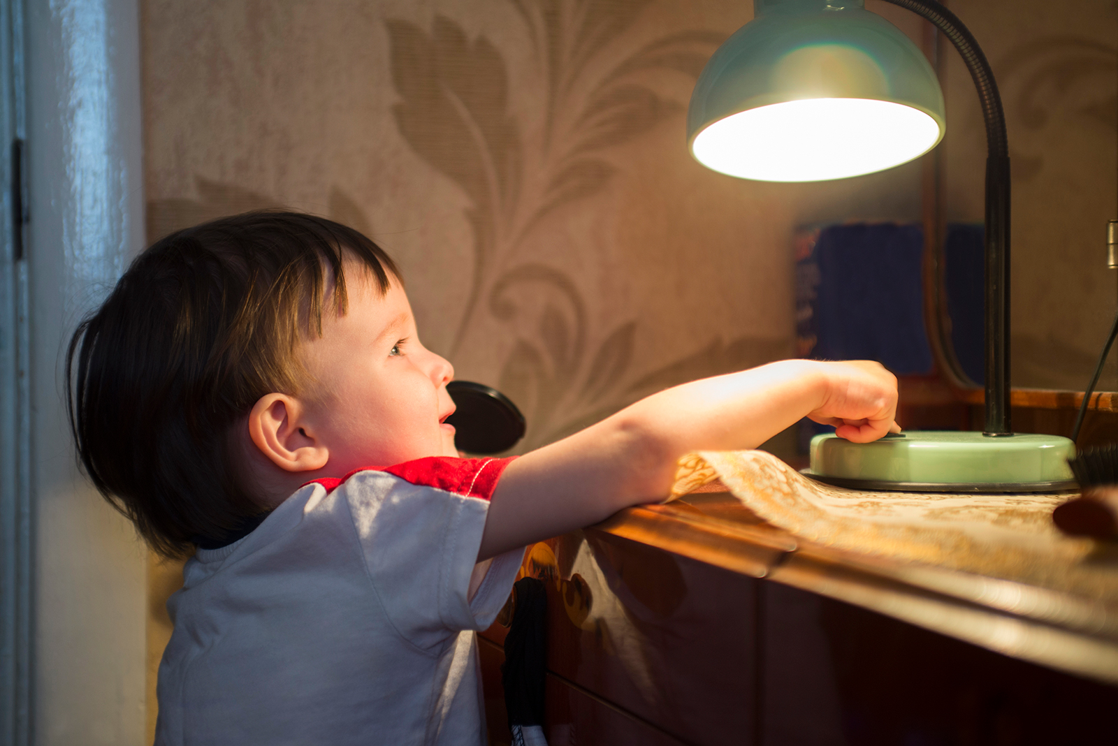 Child reaching for a lamp in a cozy room.