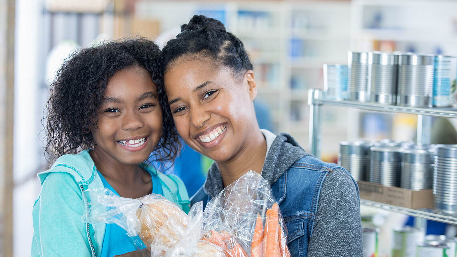 Mother and daughter smile with food donations in hand.