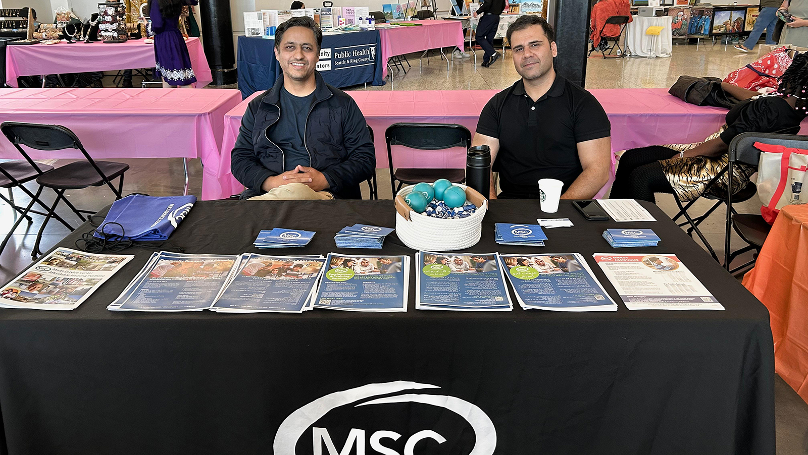 Two men at a booth with informational materials and decorations.