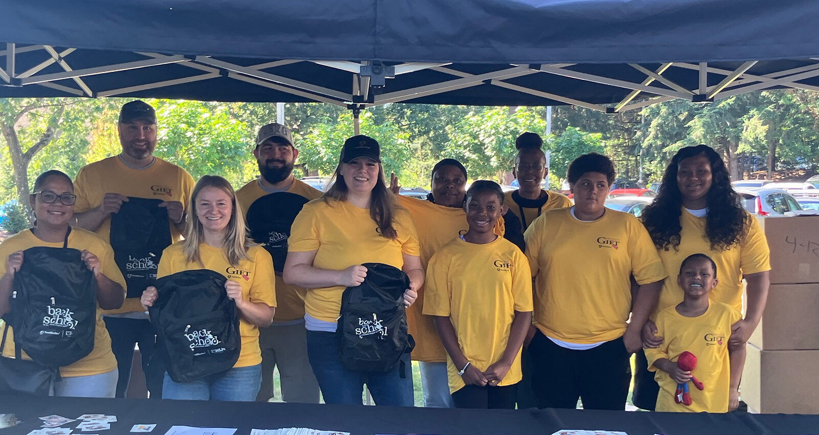 Group in yellow shirts with backpacks, outdoors at event.