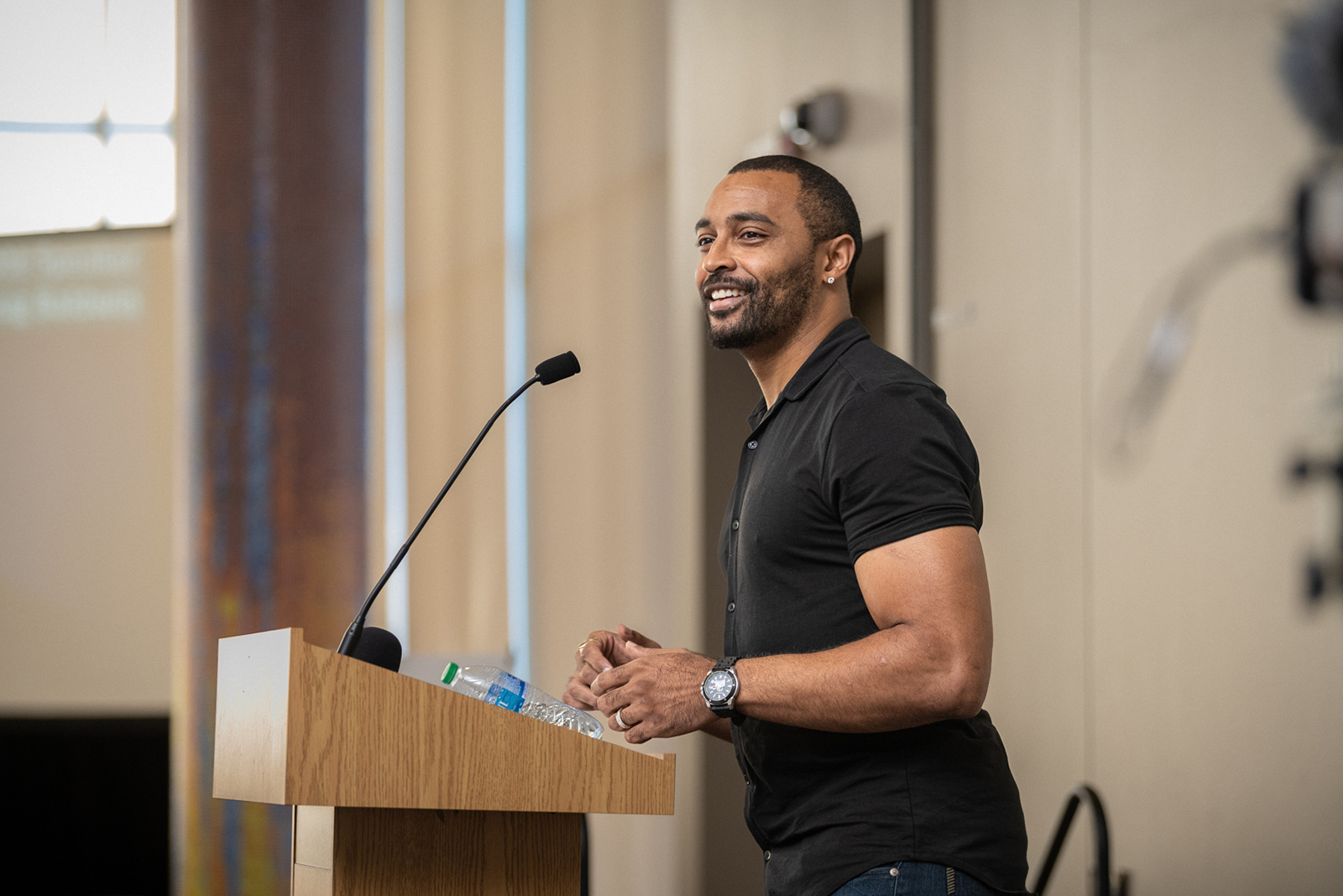 Man speaking at a podium, smiling and engaging with audience.