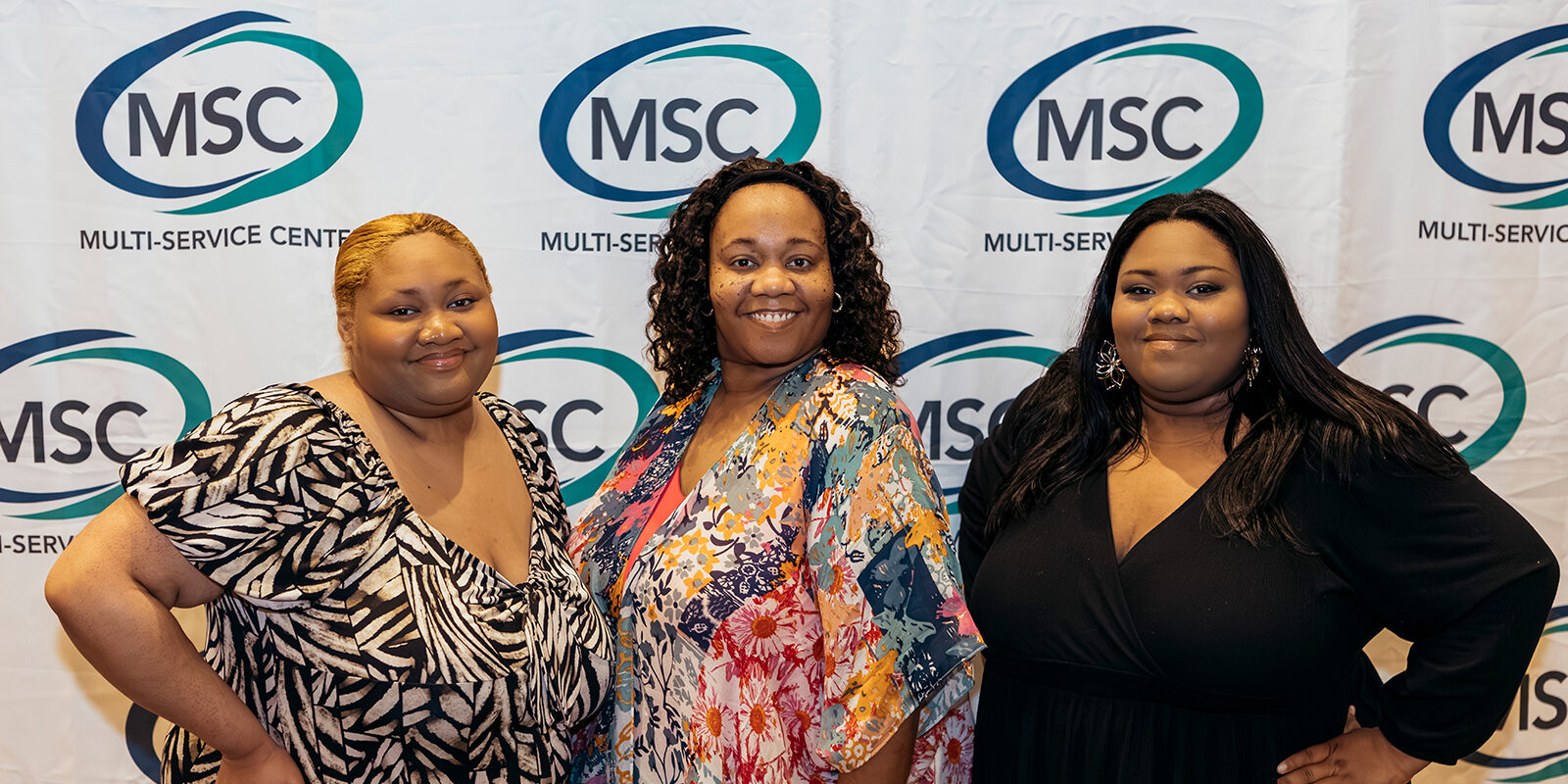 Three women posing in front of a MSC backdrop.