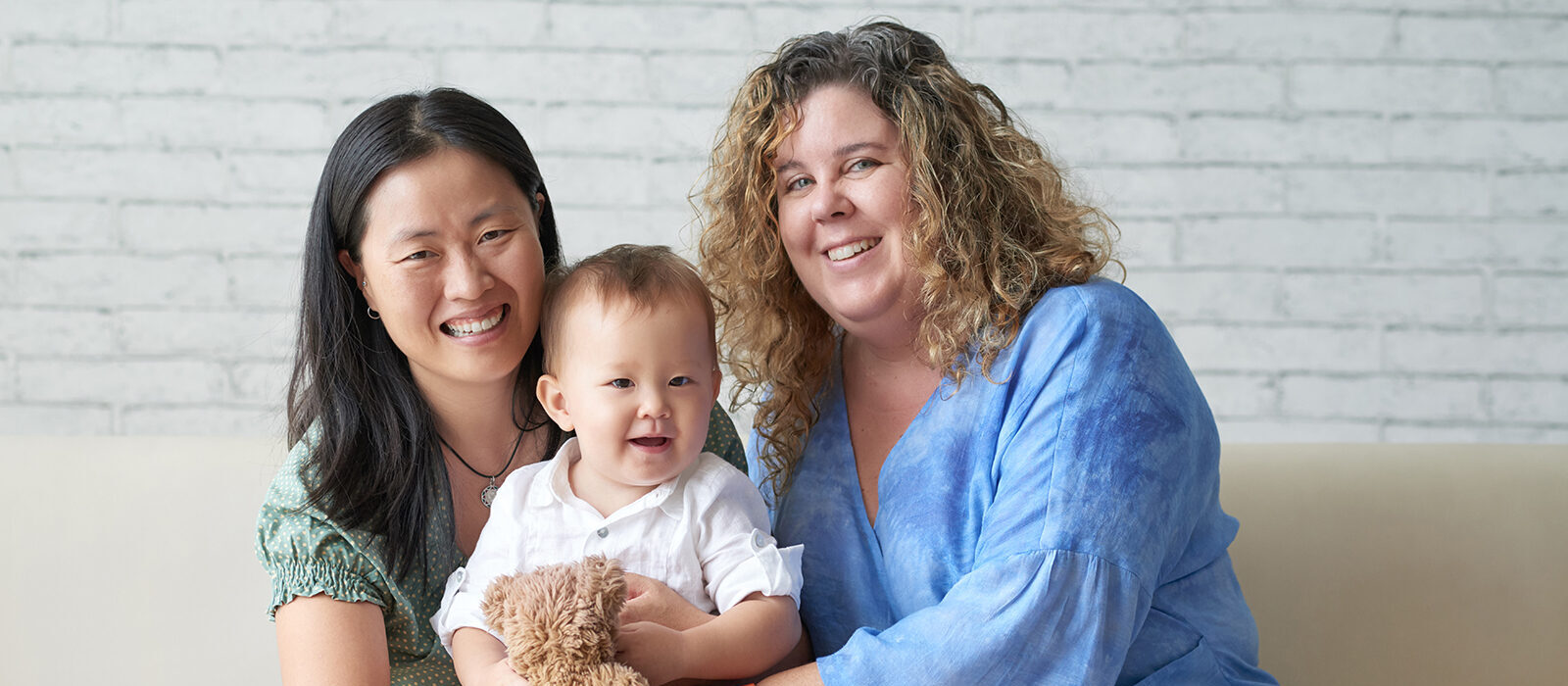 Two women and a toddler smiling together on a sofa.