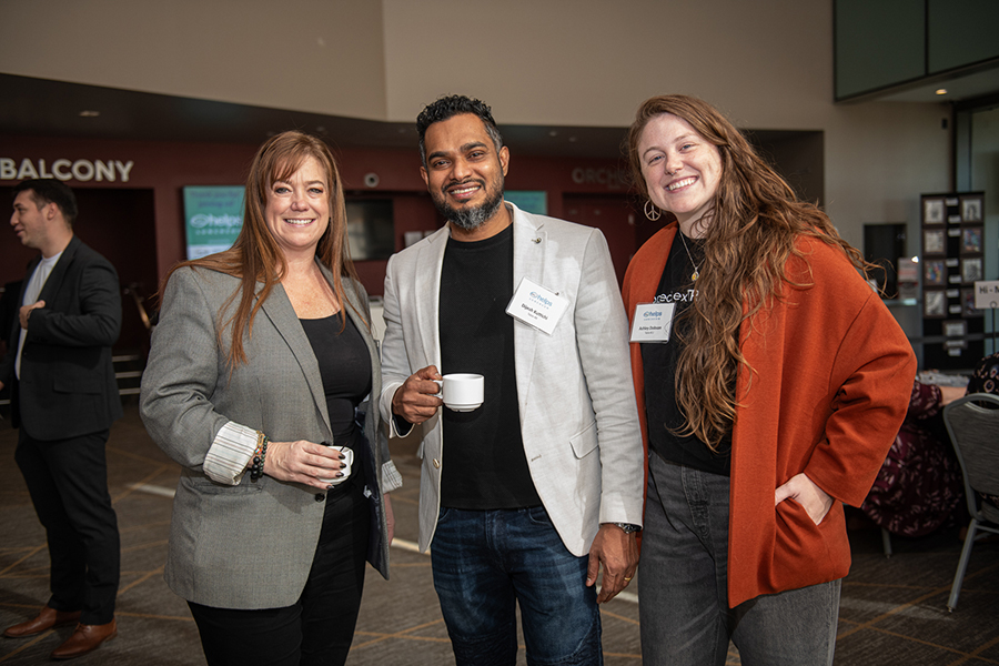 Three people smiling at an event, holding drinks.
