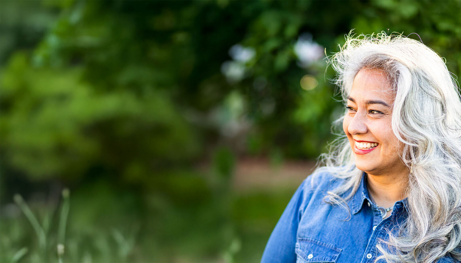 Smiling woman with silver hair outdoors in natural light.