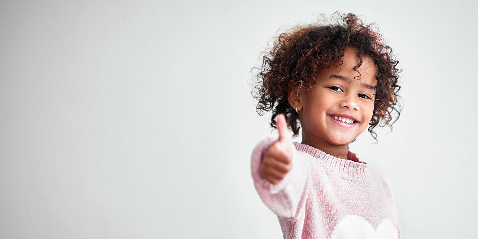 Smiling child giving a thumbs-up in cozy sweater.