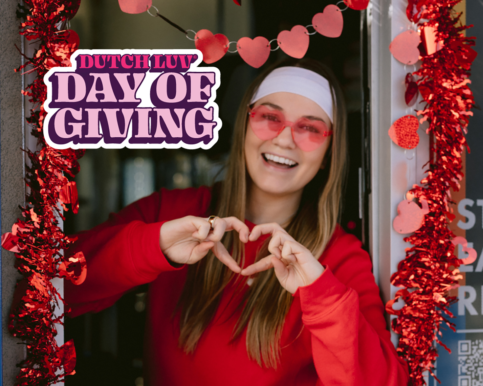 Smiling person making a heart gesture surrounded by decorations.