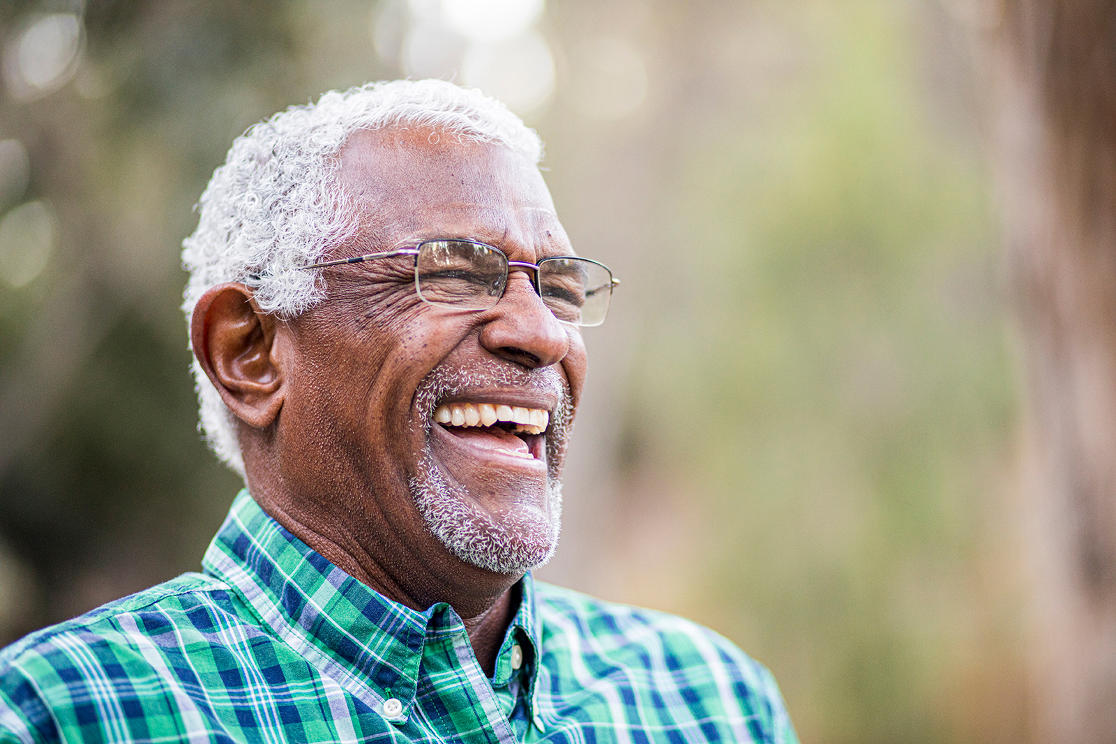Smiling older man with glasses, wearing a plaid shirt.