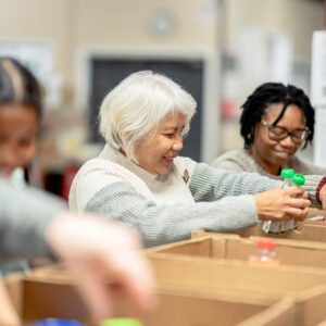Group of people organizing items in cardboard boxes smiling.