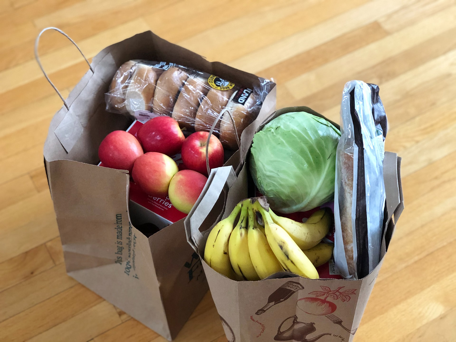 Two grocery bags filled with fruits and vegetables.
