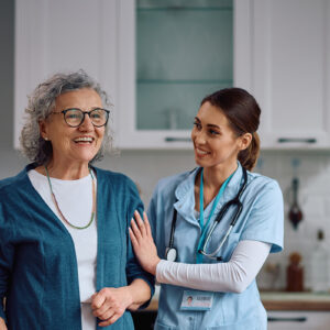 Nurse and elderly woman smiling together in a kitchen.