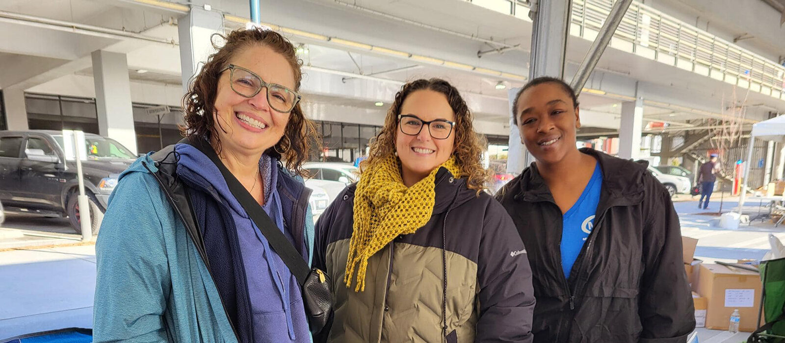 Three smiling women posing outdoors at an event.