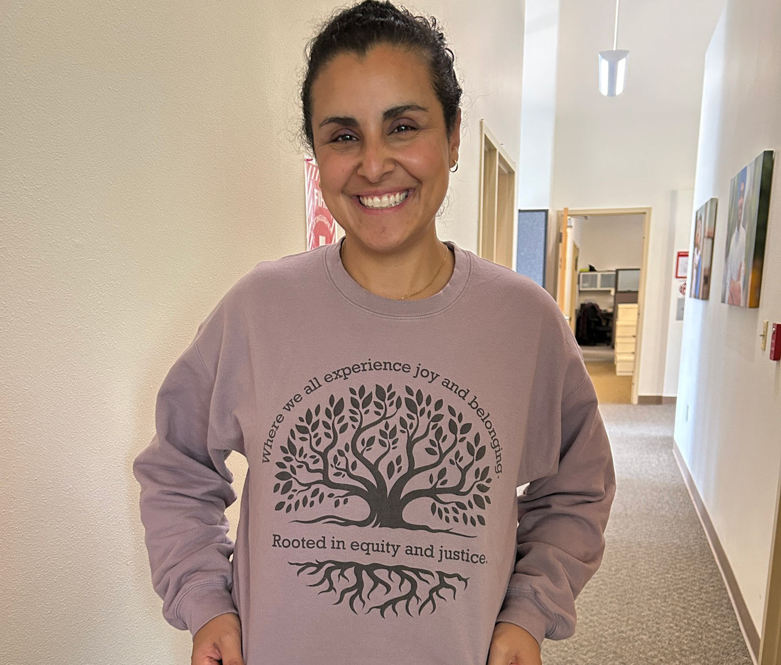 Smiling woman in a tree-themed sweatshirt, hallway background.