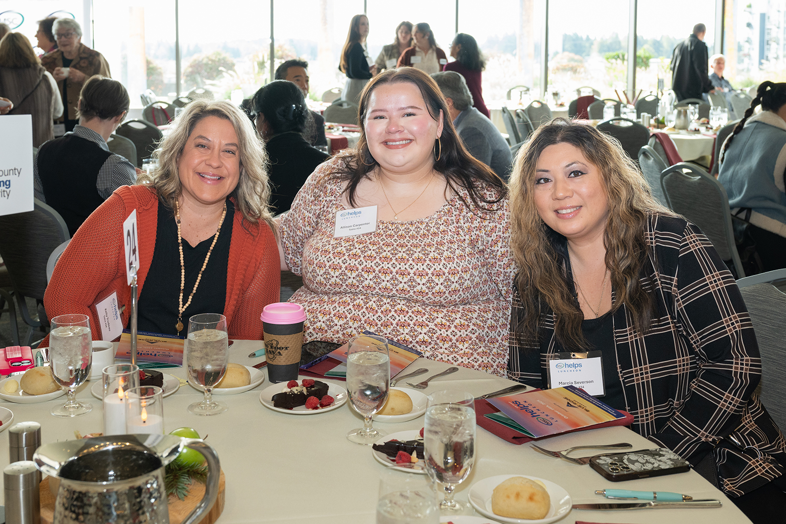 Three women smiling at a dining table event.