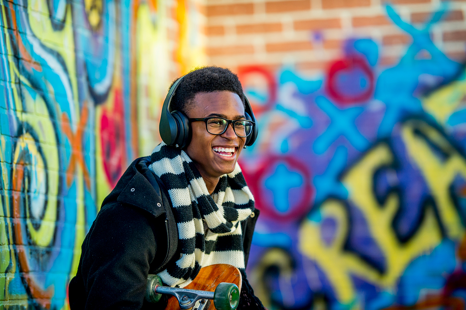 Smiling person with headphones near colorful graffiti wall.