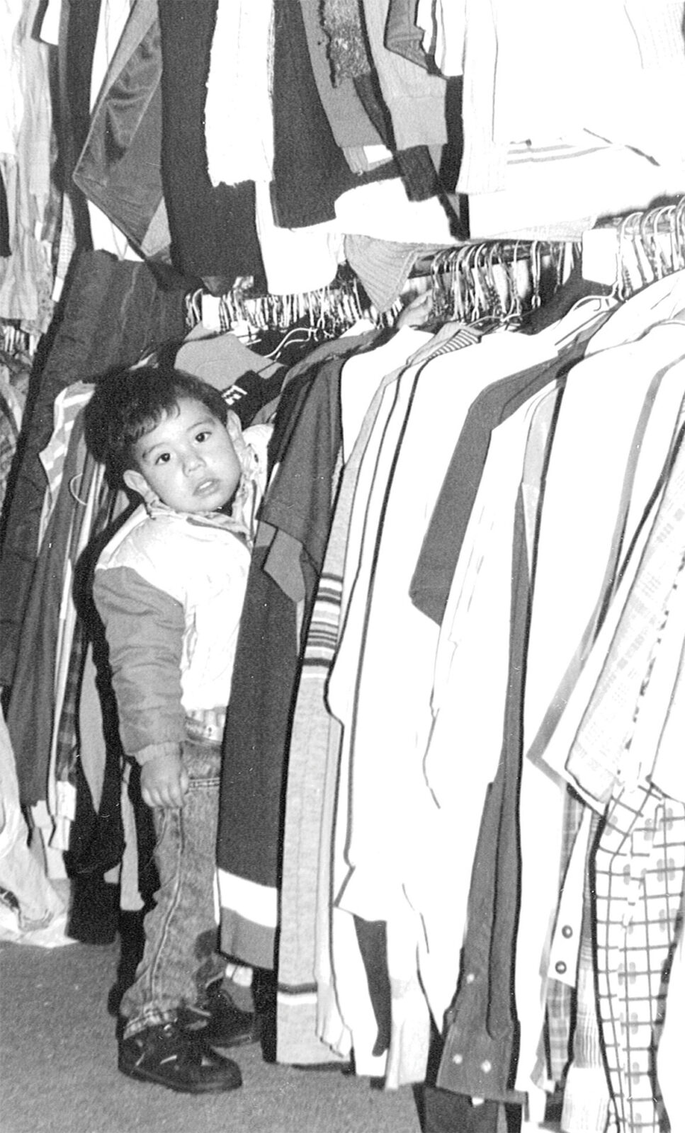 Child peeking from behind a clothing rack in store.