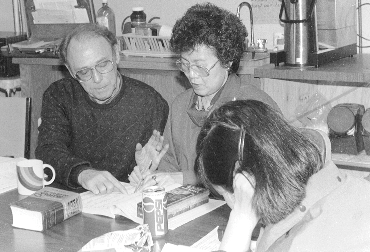 Three people engaged in discussion over papers at a table.