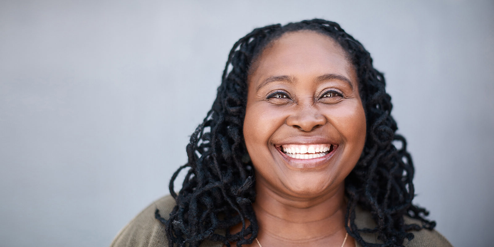 Woman smiling brightly with long, curly hair against a gray background.