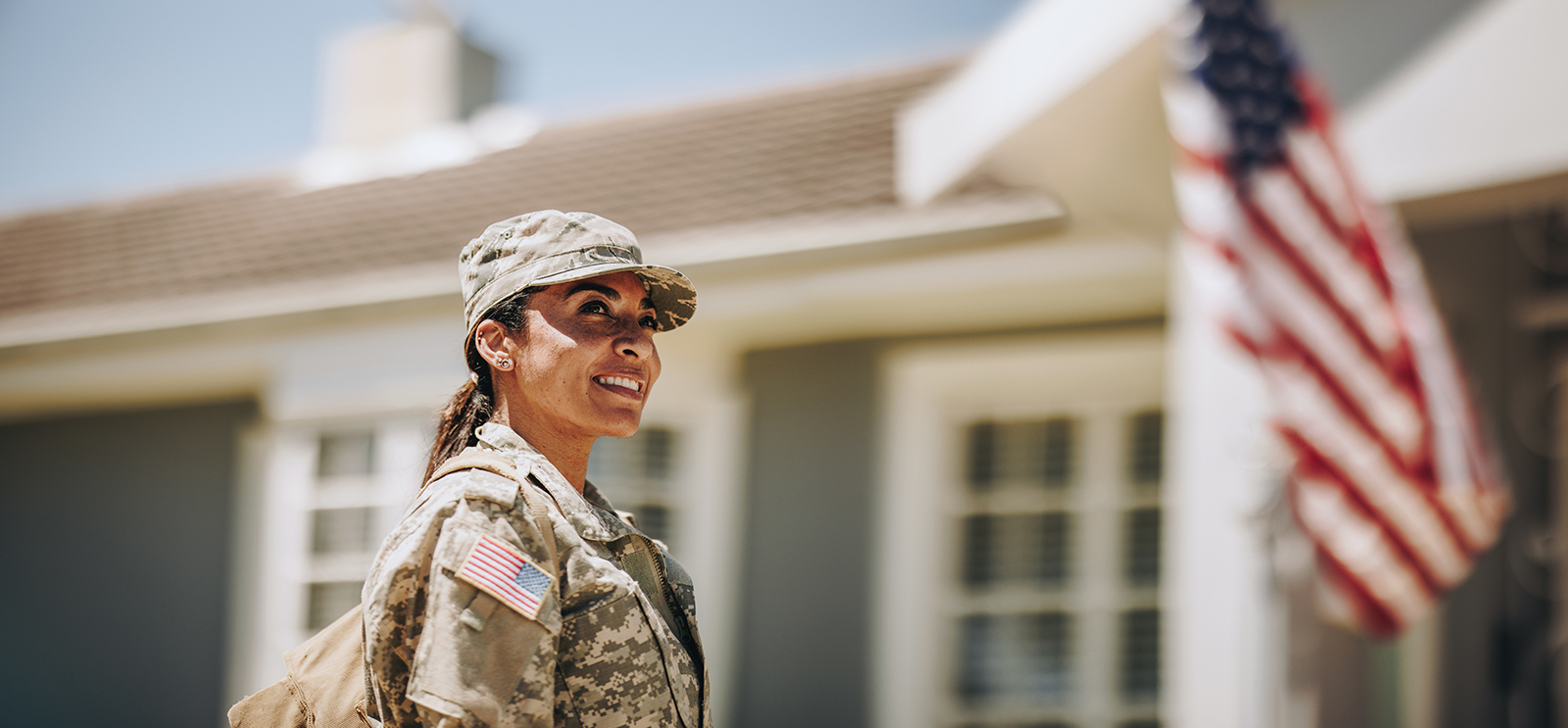Smiling soldier in uniform outside with American flag background.